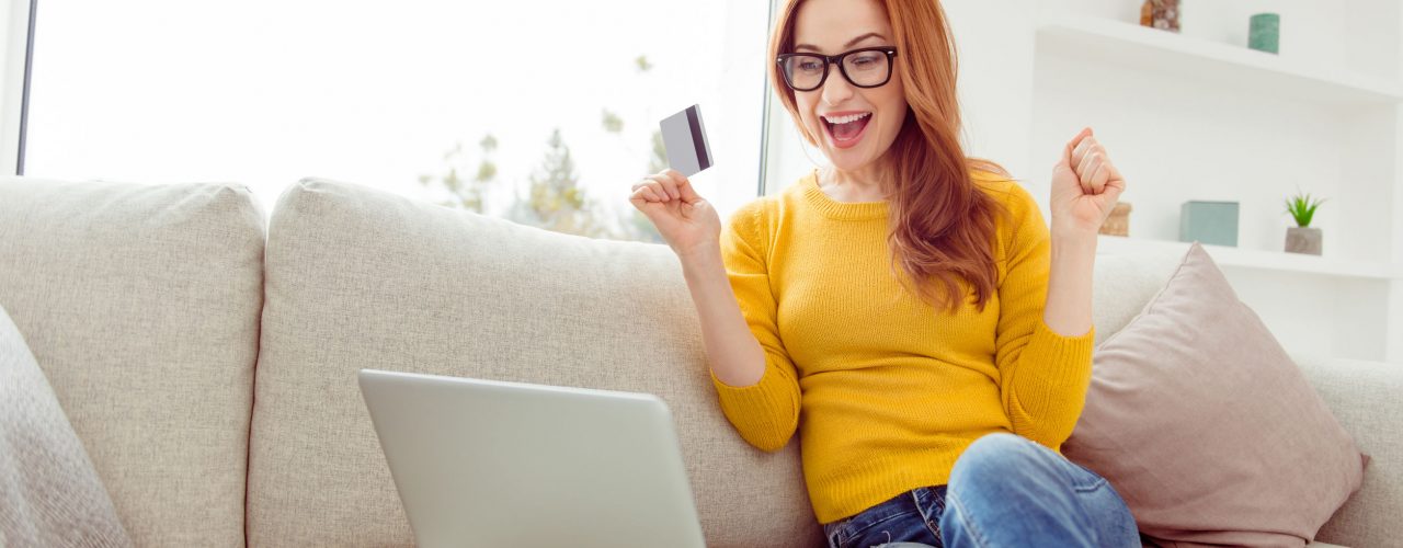 Sale discount weekend concept. Low angle top view of glad lady in spectacles sit on comfort, cozy sofa or couch in yellow sweater and denim jeans, rejoice in modern white bright interior