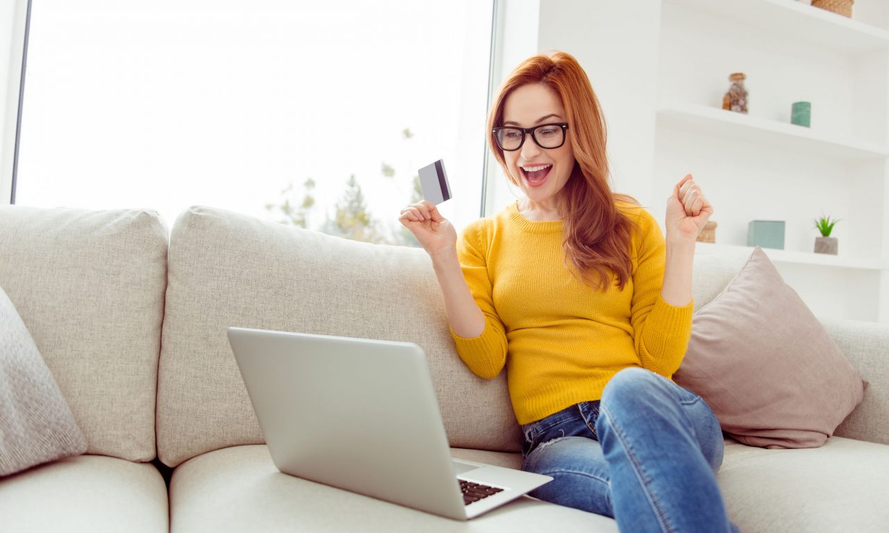 Sale discount weekend concept. Low angle top view of glad lady in spectacles sit on comfort, cozy sofa or couch in yellow sweater and denim jeans, rejoice in modern white bright interior